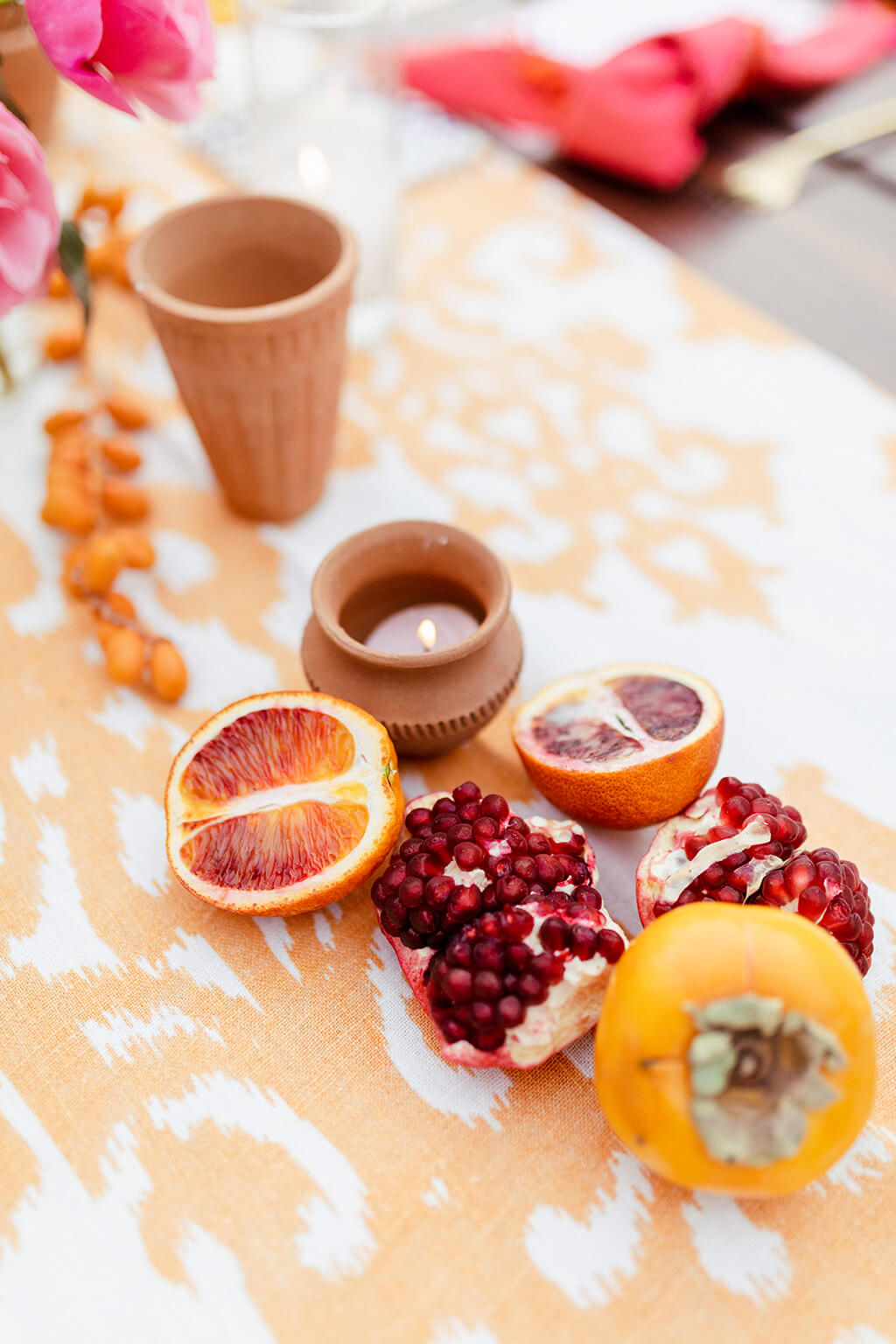 Table detail of blood oranges, pomegranate, and persimmon on an ikat runner with terracotta cups