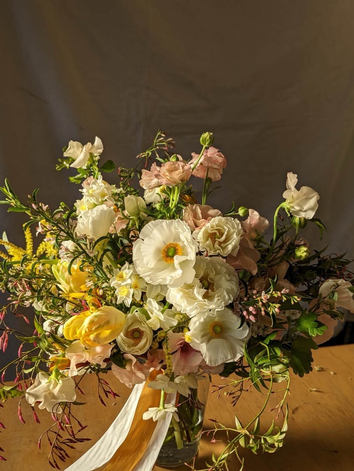 Bouquet of cream poppies, blush lisianthus, and jasmine vine against a grey backdrop