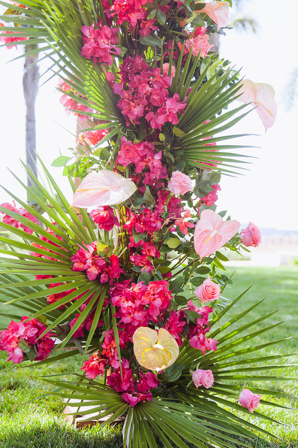Column installation of magenta bougainvillea, palm fronds, and blush anthurium