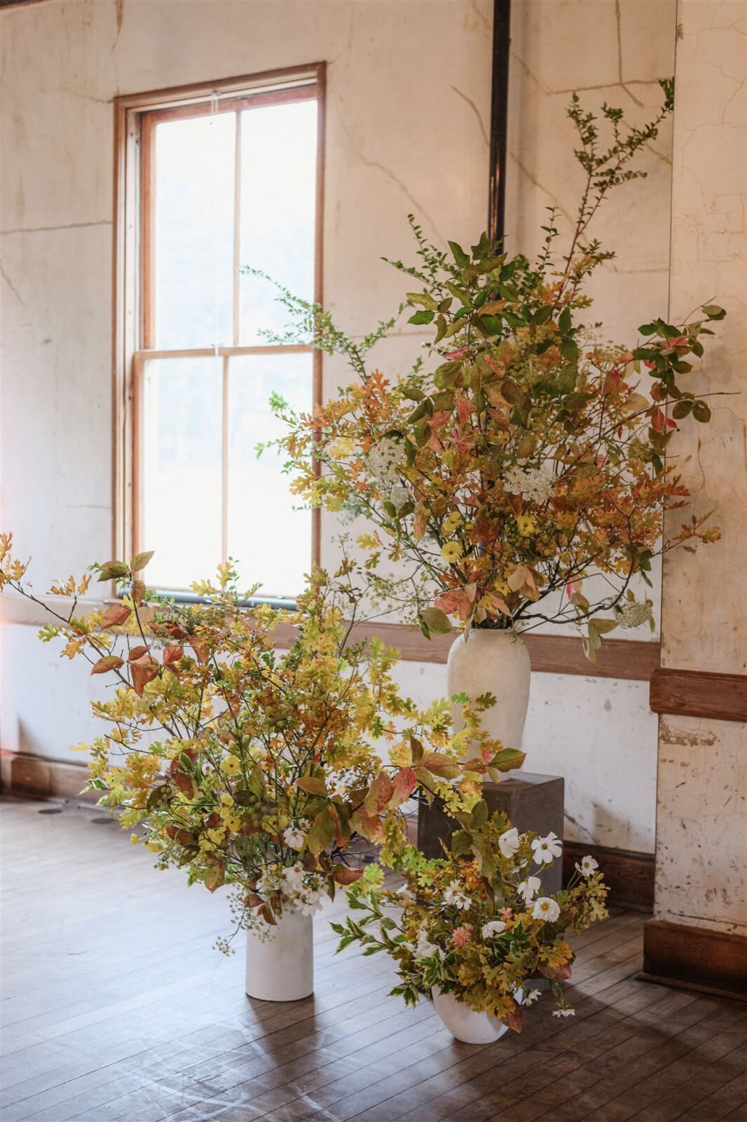 Autumn branch installation rising from white vessels in a sunlit plaster room