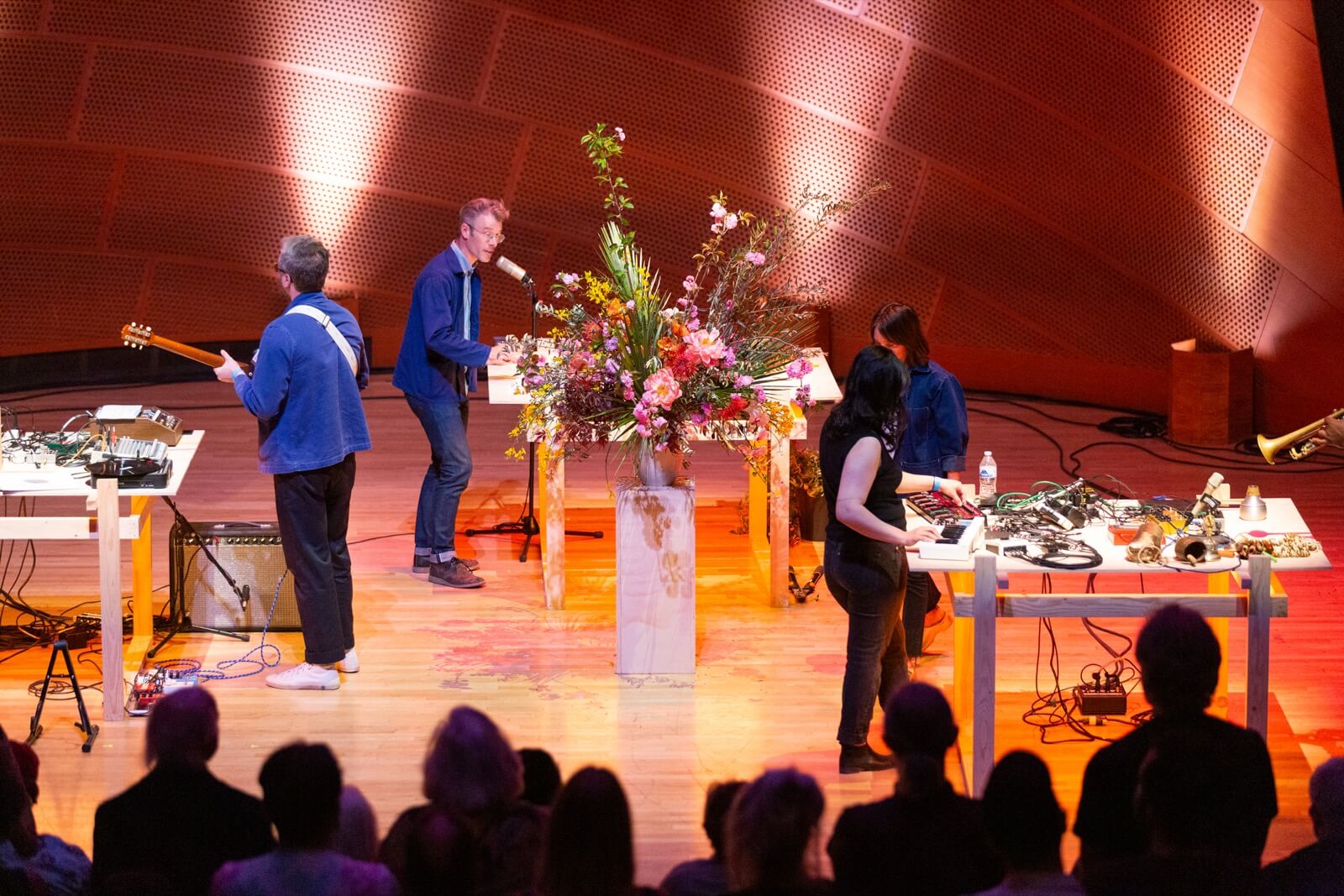 Musicians on stage at a concert hall with tall floral arrangements on white pedestals