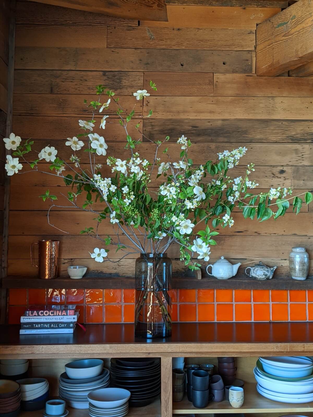 White dogwood branches in a glass vase on a kitchen shelf with orange tile