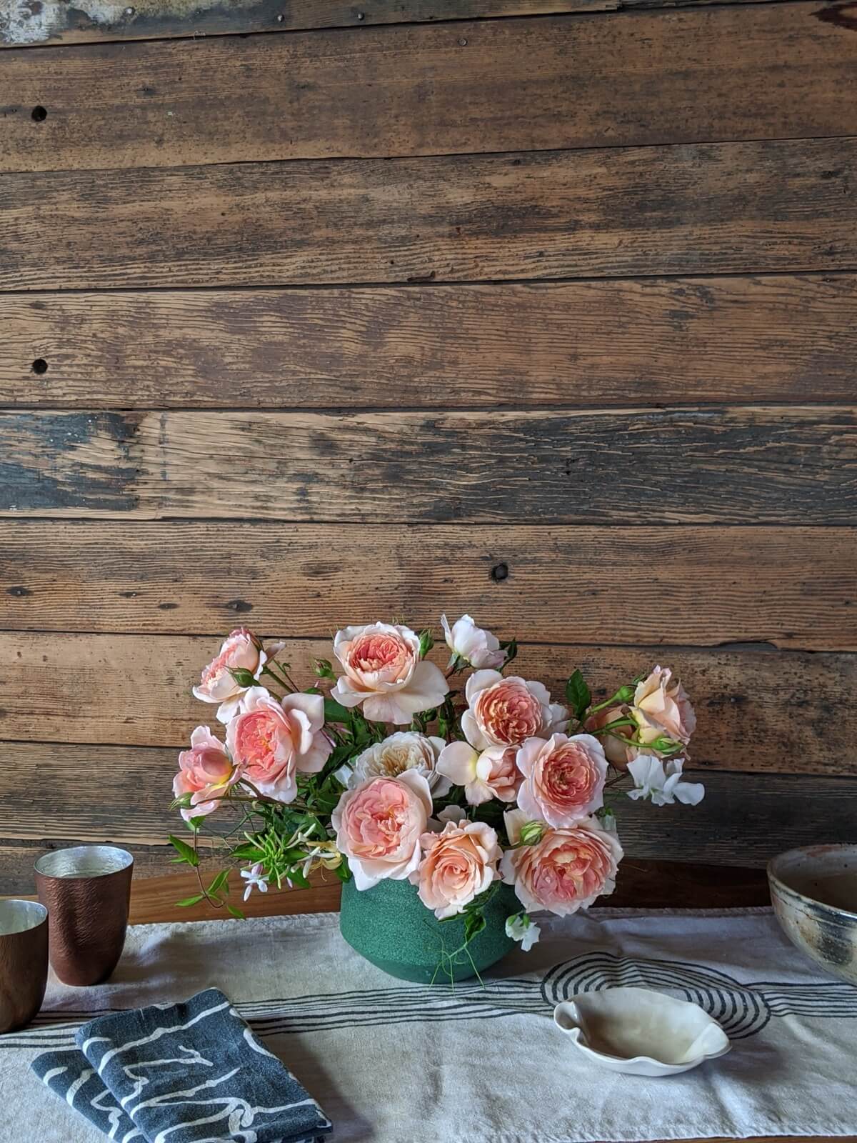 Peach garden roses and sweet pea in a green ceramic bowl against reclaimed wood