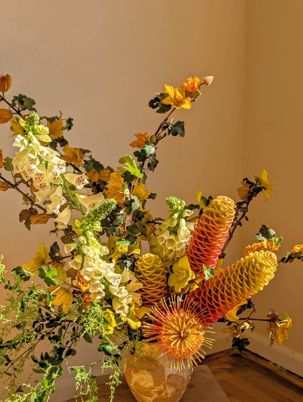 Warm arrangement of beehive ginger, foxglove, and turning autumn leaves in evening light