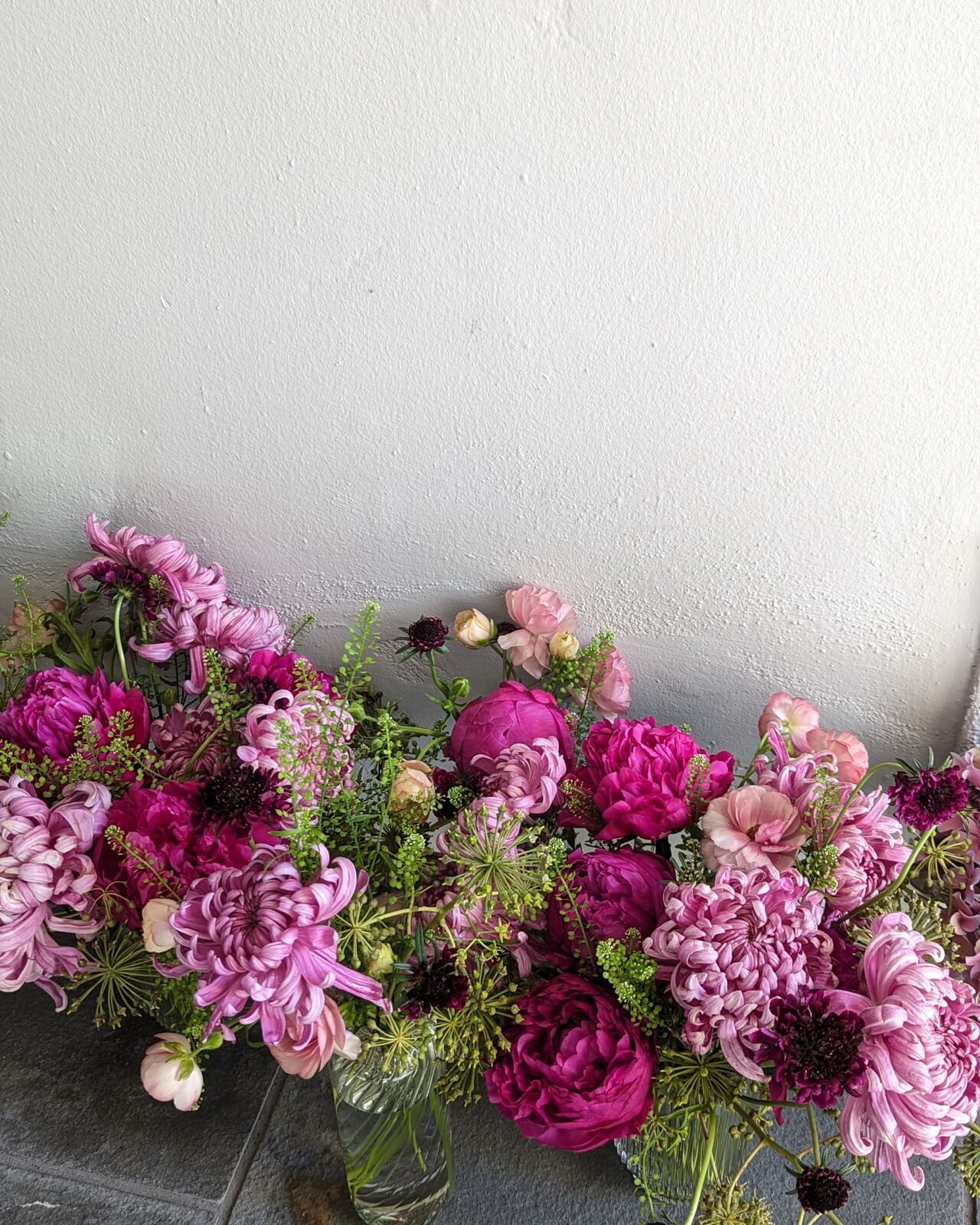 Magenta peonies, chrysanthemums, and snapdragons massed along a white plaster wall