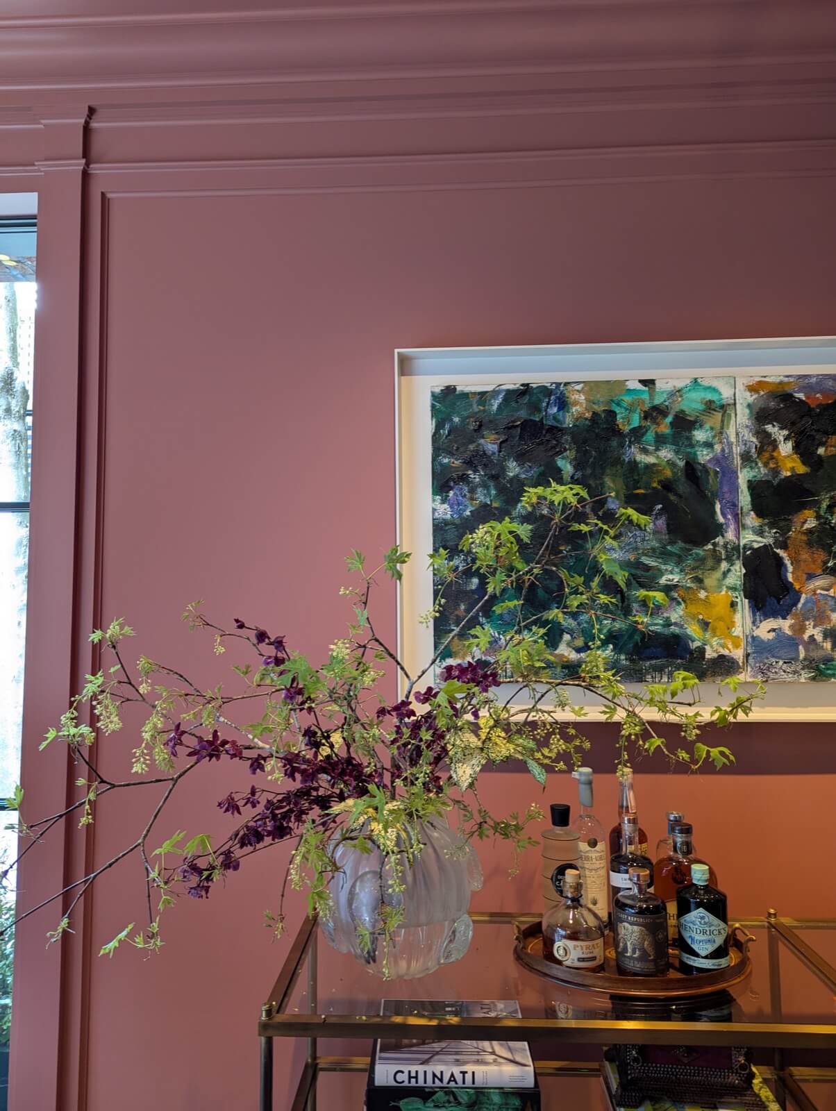 Plum branches arching from a glass vase on a bar cart against a rose-pink wall