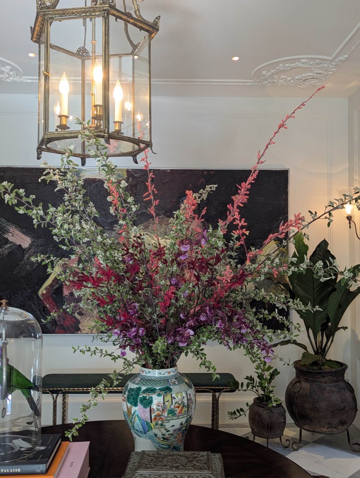 Tall magenta flowering branches in a porcelain vase beneath a lantern chandelier