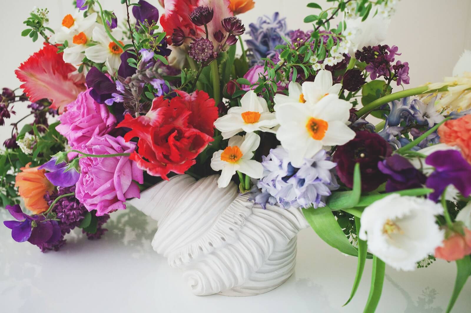 Spring arrangement of narcissus, hyacinth, tulips, and lilac in a white shell vase