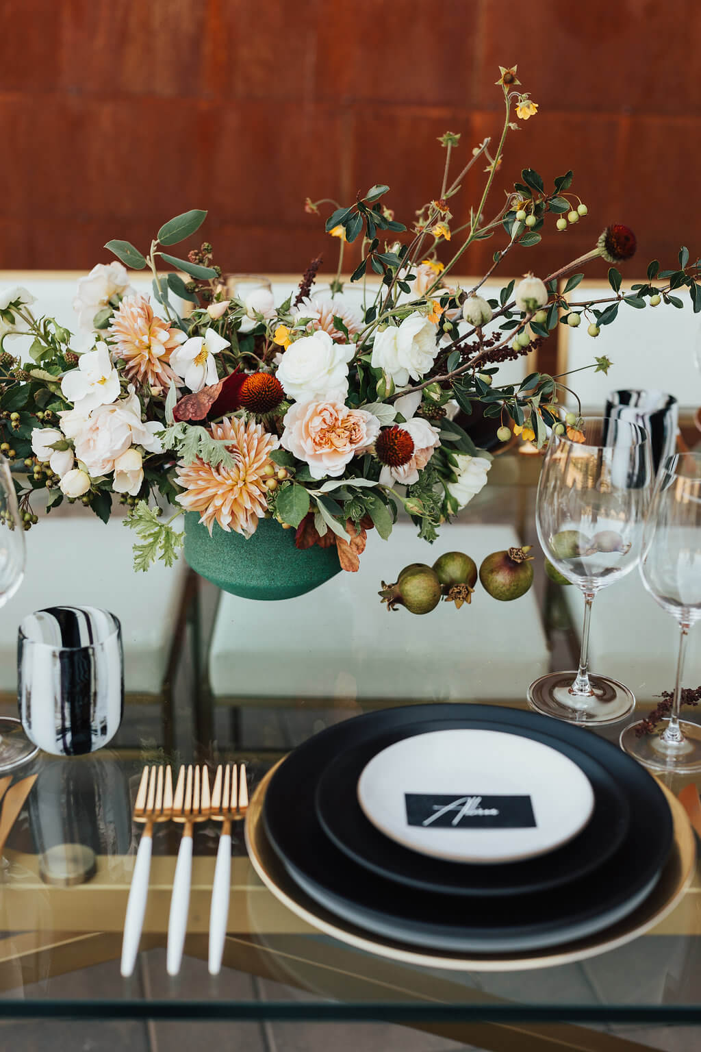 Peach and cream centerpiece with dahlias and garden roses on a glass table set with black plates and gold flatware
