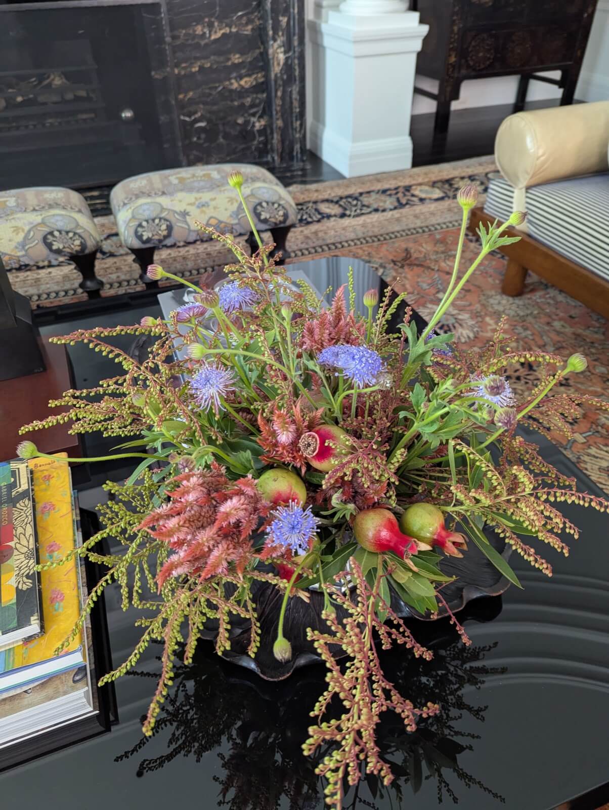Arrangement of blue ageratum, thistle, and berried branches on a black coffee table