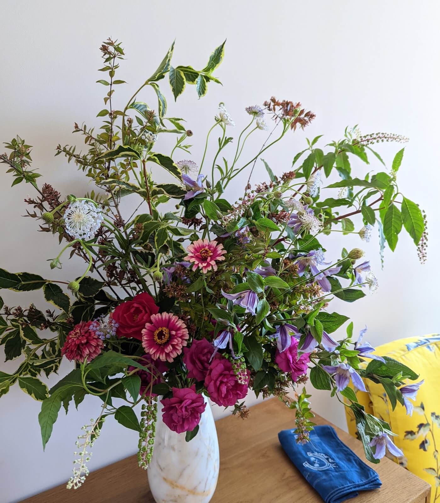 Garden gathering of zinnias, clematis, and pokeweed in a white pitcher on a wooden table